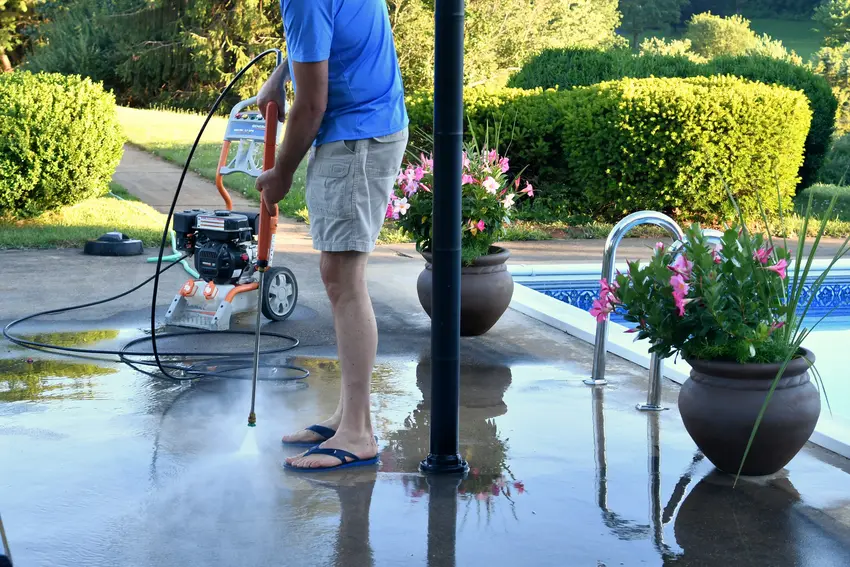 A man washing the dirt of the cement pool by pressure washing