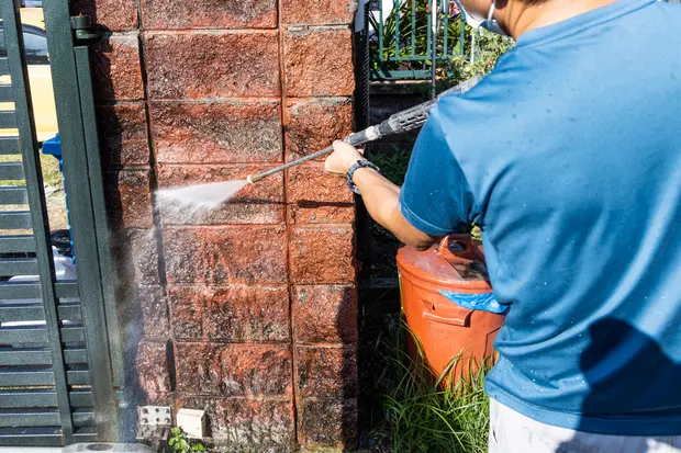 A worker cleanig wall moss at residential building with pressure washing