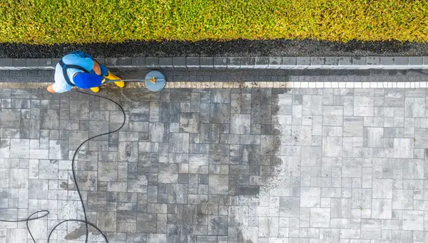 A worker cleaning a stone patio with pressure washing