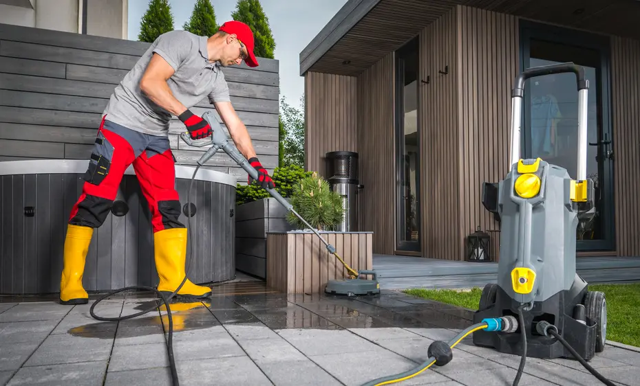 A worker washing patio concrete bricks using pressure washing