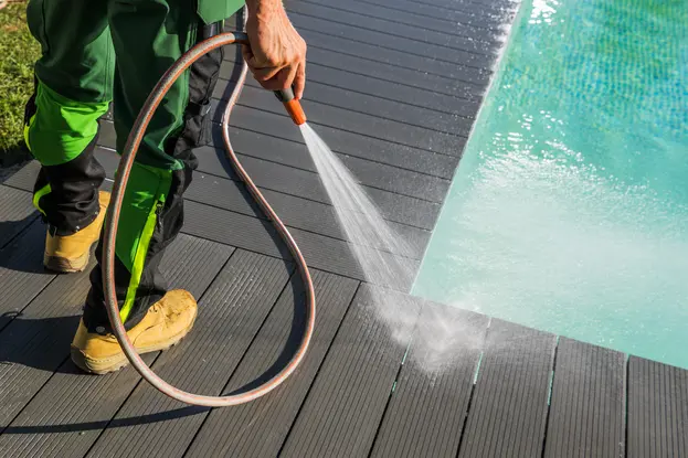 A man cleaning swimming pool deck by pressure washing