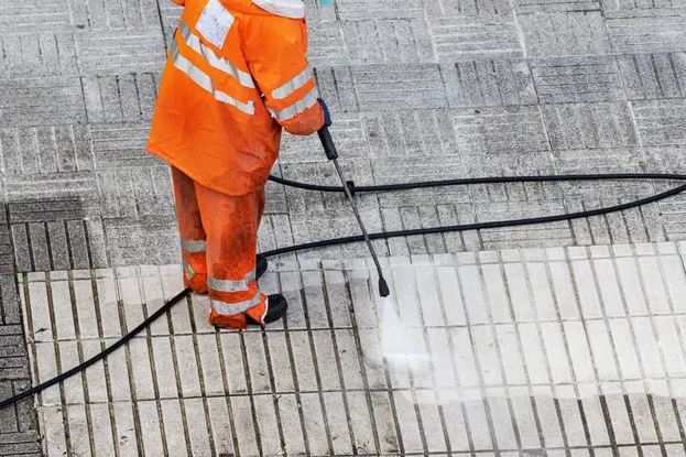 A worker cleaning street sidewalk by pressure washing