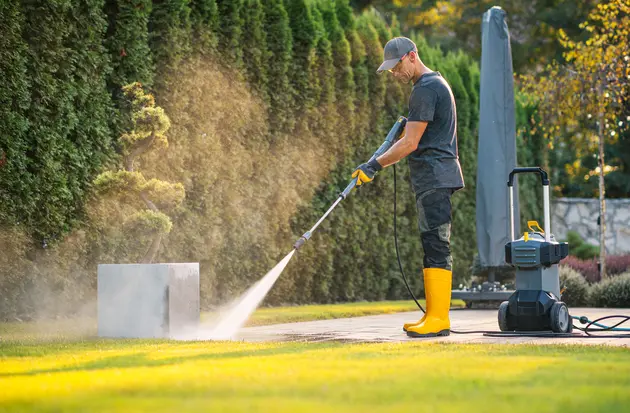 A worker pressure washing patio in garden