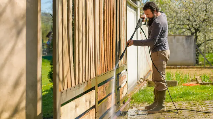 A worker cleaning fence with pressure washing tool