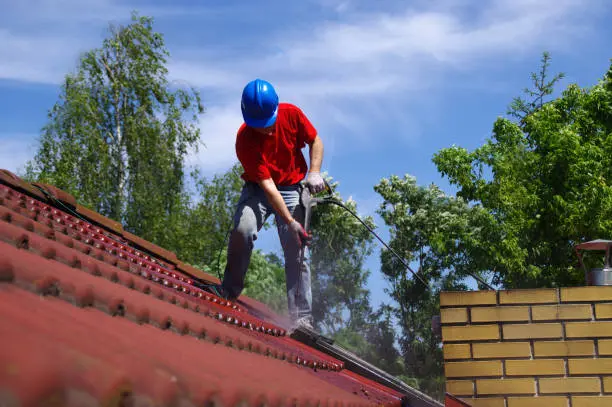 Worker cleaning roof tiles with low water pressure
